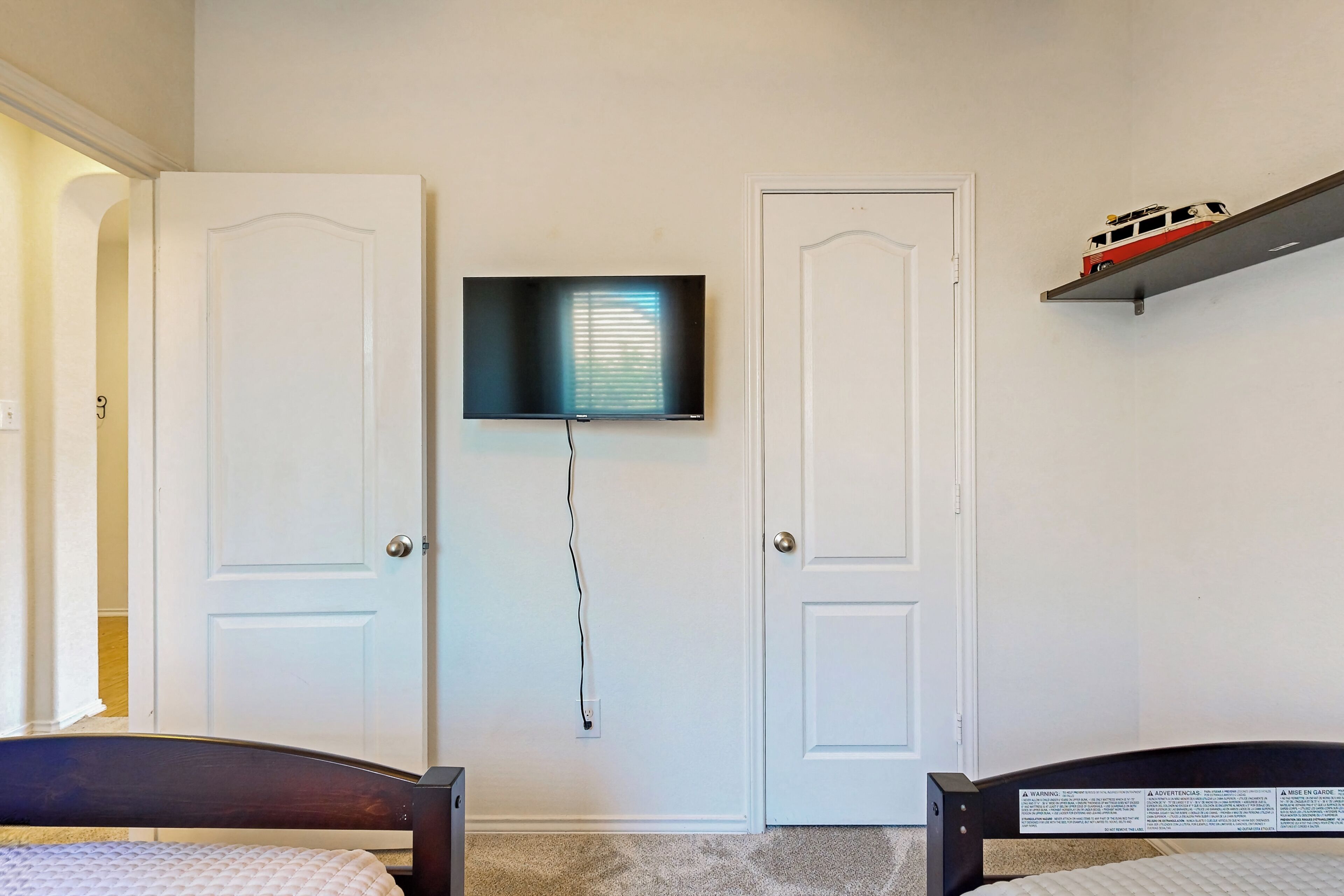Ein Schlafzimmer mit zwei Türen, einem an der Wand befestigten Fernseher und einem Regal mit einem Spielzug.