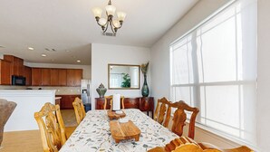 A spacious dining area with a long table and wooden chairs, a chandelier, and a large window providing natural light. - Inviting Home w/ Enlosed Yard & Gas Grill (Round Rock)