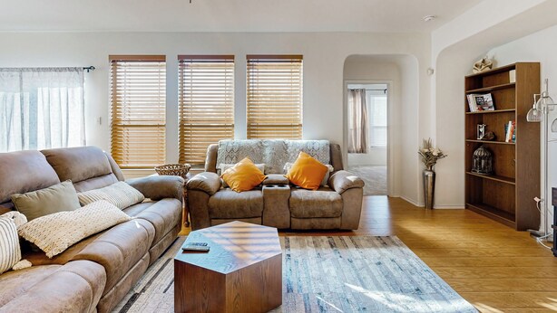 A living room with a sofa, armchair, and coffee table. There are two windows with blinds, a ceiling fan, and a bookshelf. - Inviting Home w/ Enlosed Yard & Gas Grill (Round Rock)
