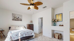 A bedroom with a bed, a ceiling fan, a dresser, a nightstand, a vase with flowers, and a framed picture on the wall. - Inviting Home w/ Enlosed Yard & Gas Grill (Round Rock)