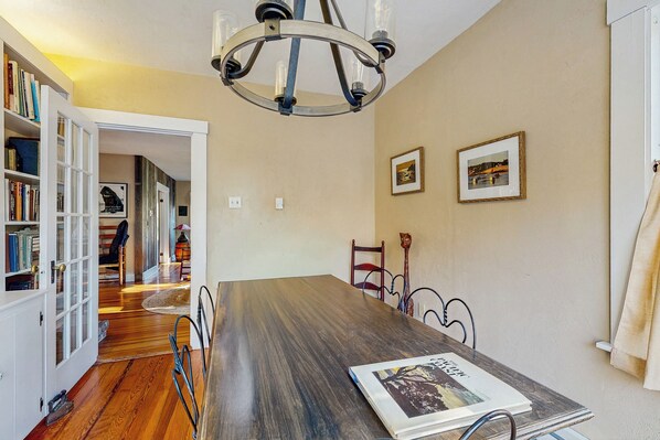 A dining area with a wooden table, chairs, a chandelier, and framed pictures on the wall. - 4BR House w/ Kitchen, Jetted Tub, Wifi + gas Grill (Orrs Island)