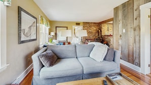 A living room with a grey sectional sofa, a coffee table, and a brick wall. - 4BR House w/ Kitchen, Jetted Tub, Wifi + gas Grill (Orrs Island)