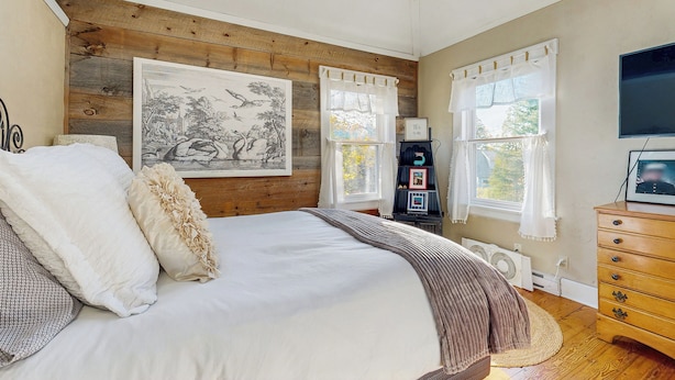 A bedroom with a large bed, wooden panel walls, a painting, a dresser, and a television. - 4BR House w/ Kitchen, Jetted Tub, Wifi + gas Grill (Orrs Island)