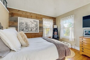 Une chambre avec un grand lit, des murs recouverts de panneaux de bois, un tableau, une commode et un téléviseur.