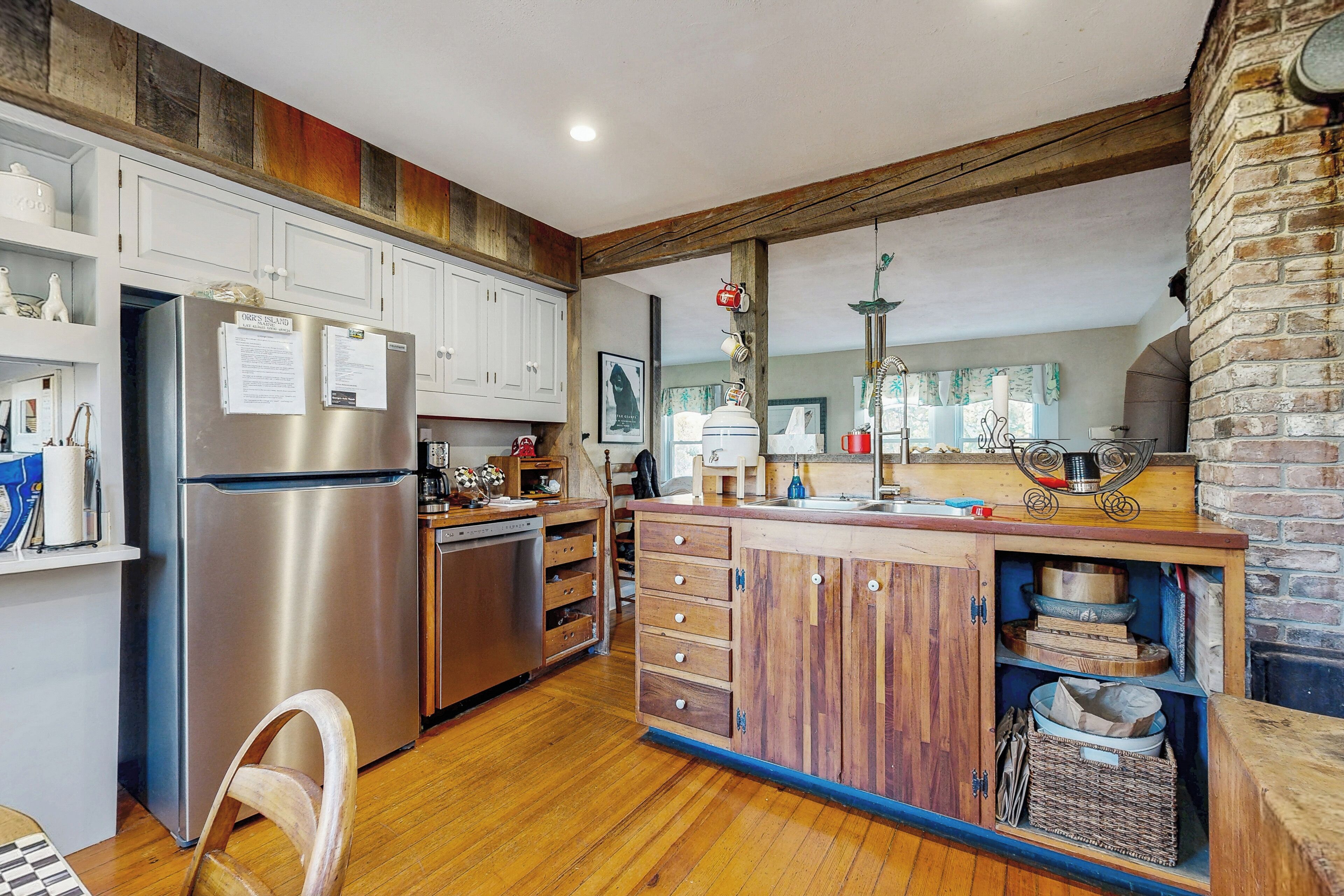 A kitchen with wooden cabinets, a stainless steel refrigerator, and a brick wall.