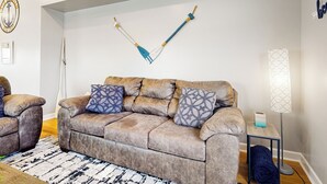 Una sala de estar con un sofá color beige, cojines estampados, una mesita auxiliar y una lámpara de pie.
