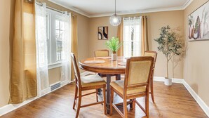 A dining room with a round wooden table, four chairs, a hanging light fixture, and a potted plant.