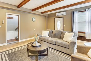 A living room with a sectional sofa, a coffee table, and a rug. There is a door leading to a hallway, and an air conditioning unit on the wall. - Inviting Family Home, 2 Mi to Eastwood Mall! (Niles)