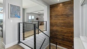 A modern interior with a wooden accent wall, a staircase with metal railings, and a dining area in the background. - Waterfront Home on Lake LBJ w/ Pool & Dock! (Kingsland)