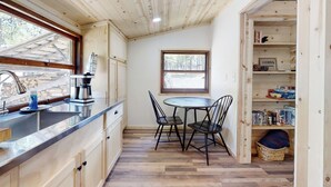 A compact kitchen with a wooden ceiling, a dining table with chairs, a window, and a built-in bookshelf.