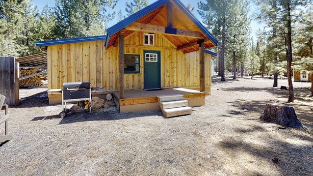 A wooden cabin with a blue roof, a front door, and a small porch.