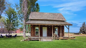 A rustic wooden cabin with a porch, surrounded by a well-maintained lawn and trees. - 1 BR Bunk House on Long Hollow Ranch, Dog Friendly (Sisters)