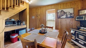 A wooden interior with a dining table, chairs, a kitchen area with a stove, and a staircase. - 1 BR Bunk House on Long Hollow Ranch, Dog Friendly (Sisters)