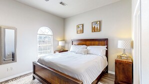 A bedroom with a large bed, a wooden headboard, two bedside tables with lamps, a mirror, and a window with blinds. - 3 Mi to Downtown Conroe: Updated Townhome w/ Yard (Conroe)