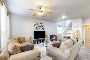 A modern living room with a large flat-screen TV, two sofas, a coffee table, and a ceiling fan. - 3 Mi to Downtown Conroe: Updated Townhome w/ Yard (Conroe)