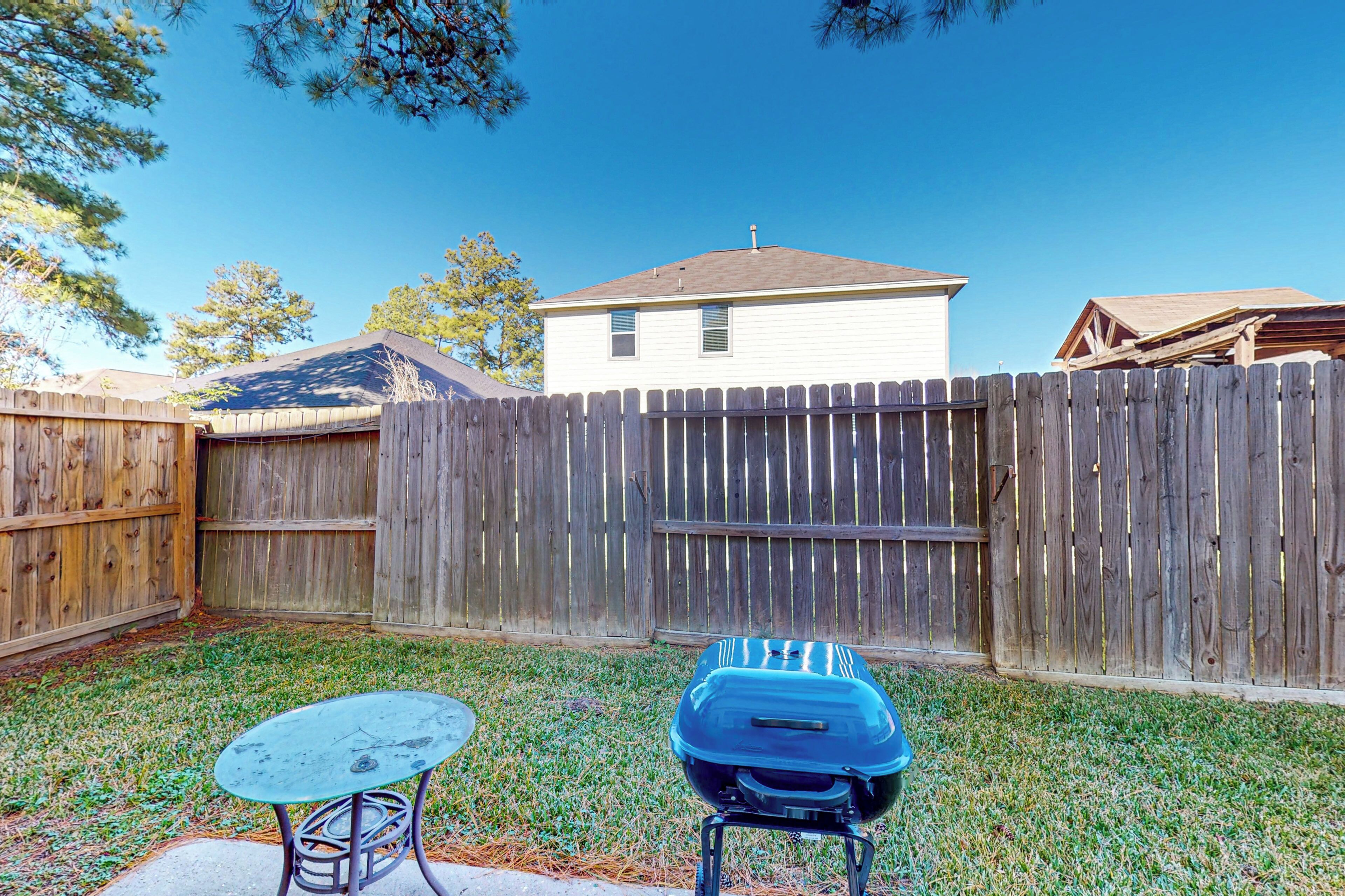 A backyard with a wooden fence, a barbecue grill, and a table.