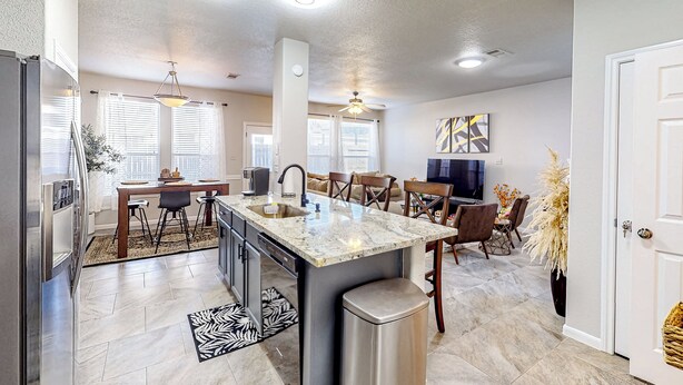 A modern kitchen with a central island, stainless steel appliances, and a dining area with a TV and seating. - 3 Mi to Downtown Conroe: Updated Townhome w/ Yard (Conroe)