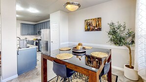 A modern kitchen with blue cabinets, a central island, and a dining area with a glass table and chairs. - 3 Mi to Downtown Conroe: Updated Townhome w/ Yard (Conroe)