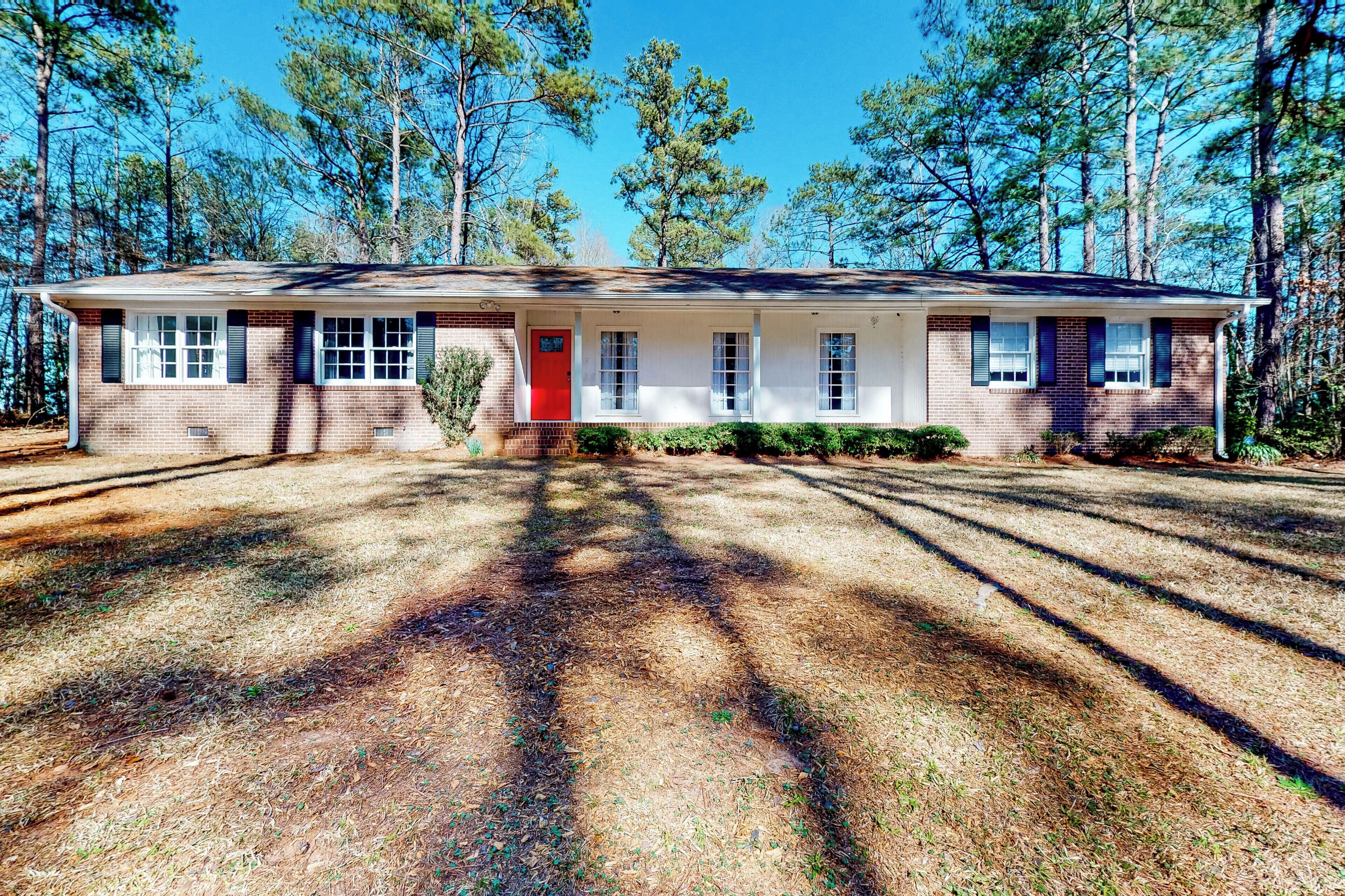 A single-story house with a red door, white siding, and a brick foundation.