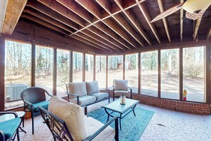 Un espacio de estar al aire libre cubierto con techo de madera, amplias ventanas y vistas al bosque circundante.