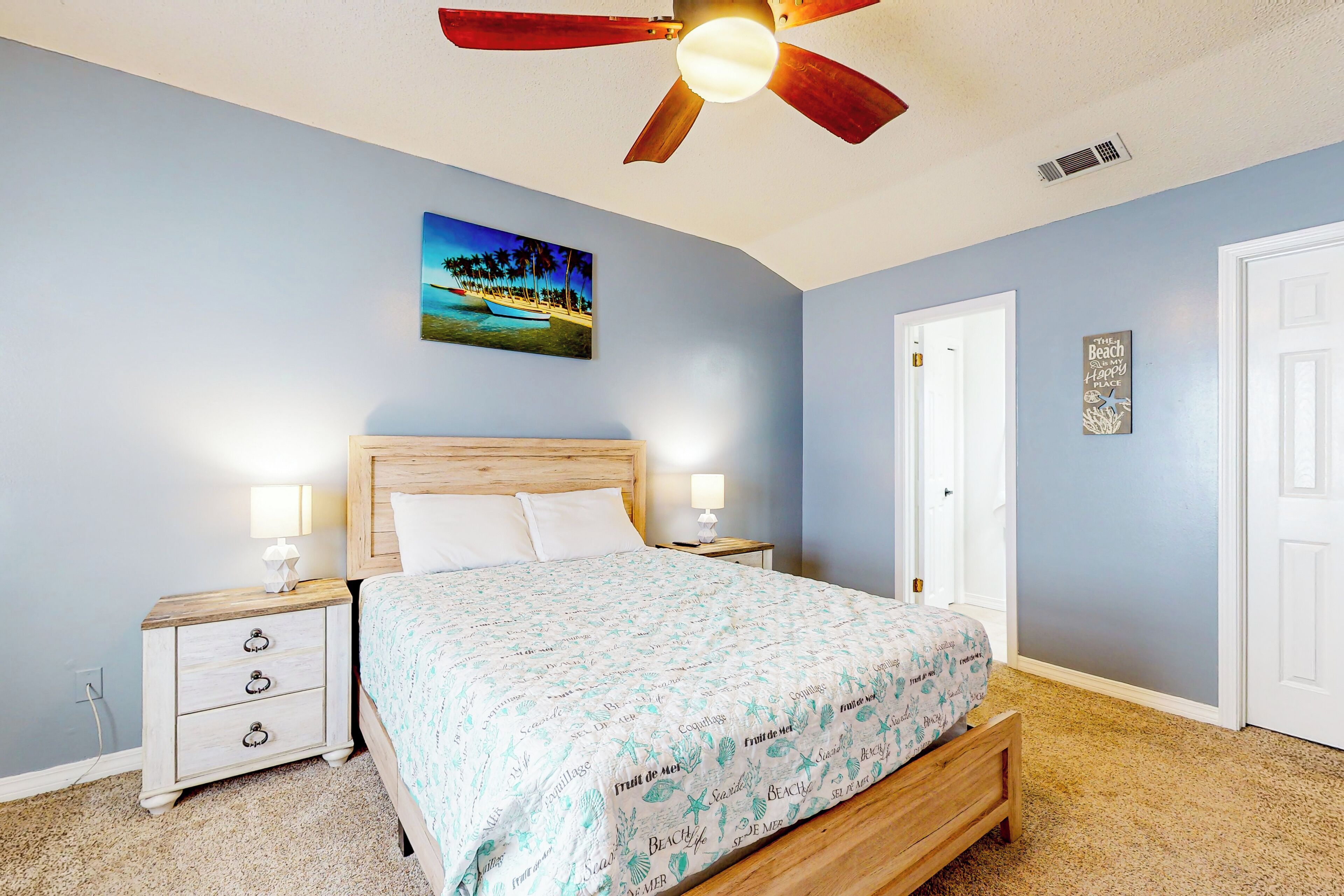 Une chambre à coucher avec un lit, des tables de chevet, un ventilateur de plafond, un tableau et une porte.