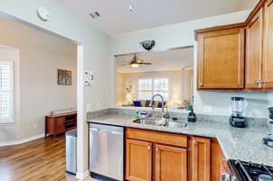 A kitchen with wooden cabinets, a granite countertop, a dishwasher, a stove, and a ceiling fan.