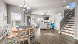 A spacious living area with a dining table, chairs, a chandelier, a ceiling fan, and a staircase. - Fort Morgan beachside retreat ~ pet-friendly ~ close to the sand (Gulf Shores)