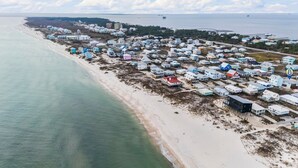 An aerial view of a coastal residential area with houses along the beach, a pier extending into the water, and a distant ship. - Fort Morgan beachside retreat ~ pet-friendly ~ close to the sand (Gulf Shores)