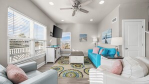 A living room with a blue sofa, white armchairs, a coffee table, and a ceiling fan. - Fort Morgan beachside retreat ~ pet-friendly ~ close to the sand (Gulf Shores)