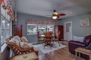Un salon avec un plancher en bois, un ventilateur de plafond, une table à manger avec des chaises, un canapé et un fauteuil en cuir.