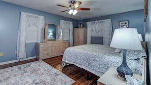 Une chambre à coucher comprenant un lit, une commode, une coiffeuse et un ventilateur de plafond.
