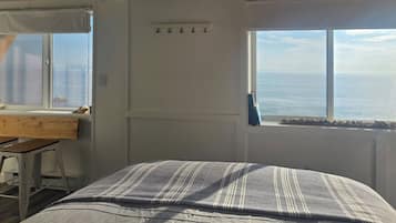 A bedroom with a bed, a desk, and a view of the sea.
