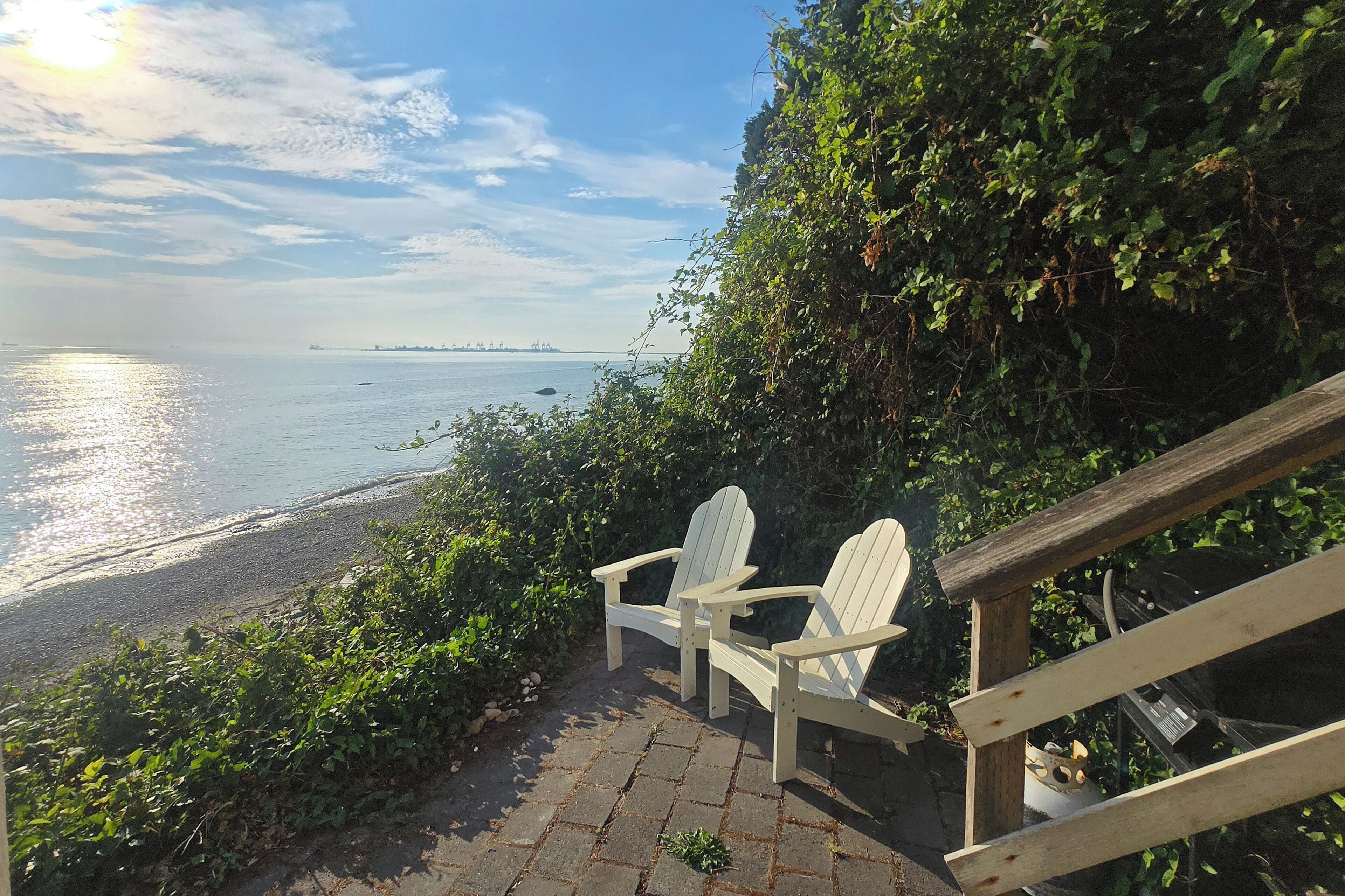 A wooden staircase leading to a beach with two Adirondack chairs.