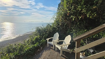 A wooden staircase leading to a beach with two Adirondack chairs.