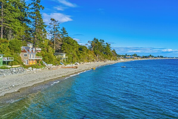 Propiedad costera con una casa que domina una playa, rodeada de un bosque frondoso.