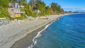 Ein Küsteneigentum mit einem großen Haus, einer Holzterrasse und einem felsigen Strand.