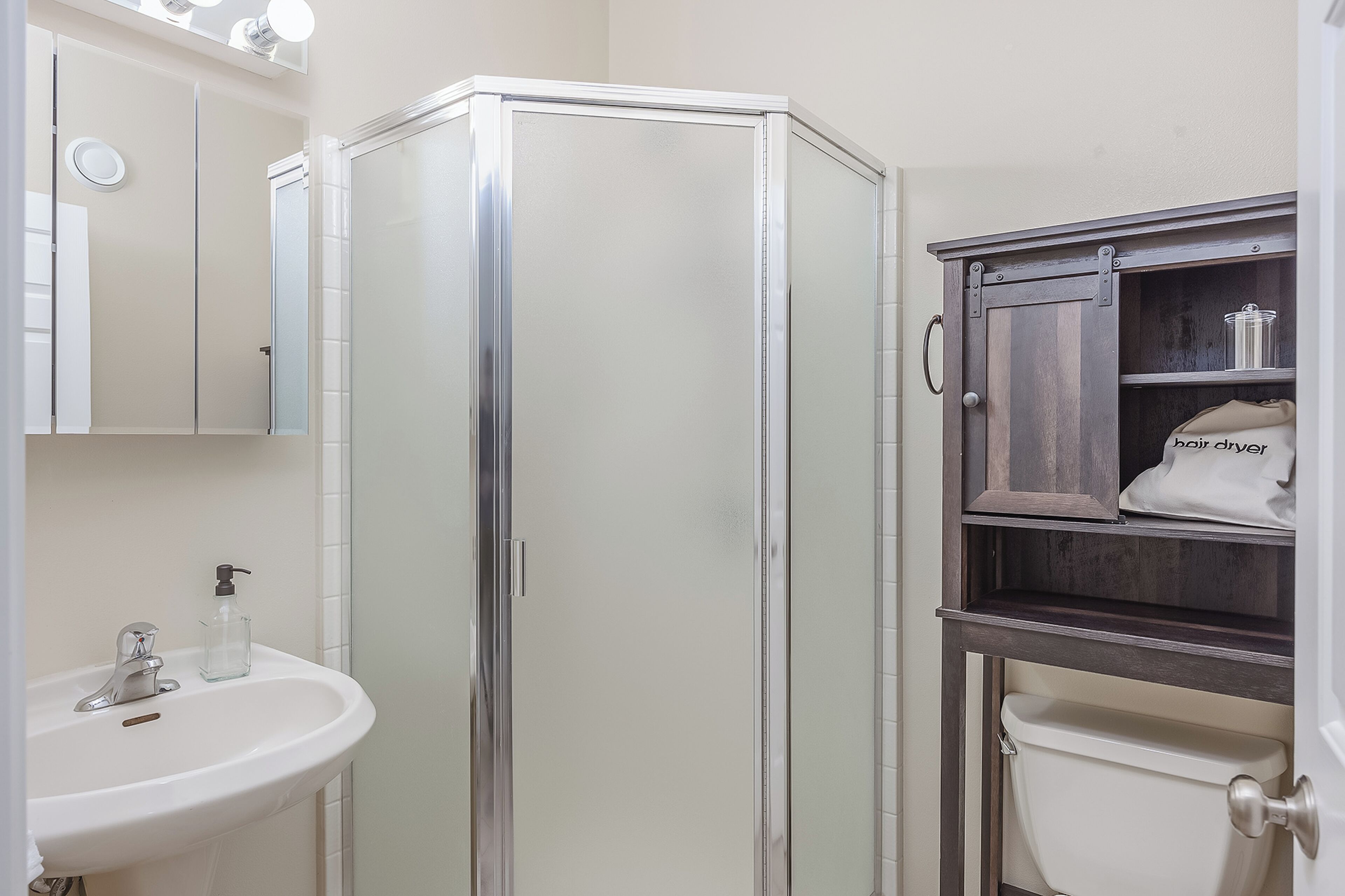 Une salle de bain avec un lavabo blanc, une cabine de douche en verre et un meuble contenant des articles de toilette.
