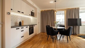 A modern kitchen with white cabinets, a microwave, and a coffee maker. There is a dining area with a table and chairs, and a TV on the right.