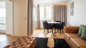 A modern living room with a leather sofa, a dining table with chairs, and a large window with curtains.