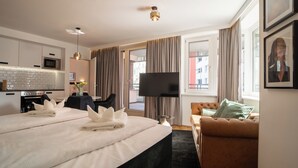 A hotel room with a bed, a TV, a sofa, and a dining area.