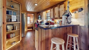A wooden interior with a kitchen area, wooden shelves, and a bar stool. - Water-view Cabin w/ Front Porch, W & D, Streaming (Carmine)