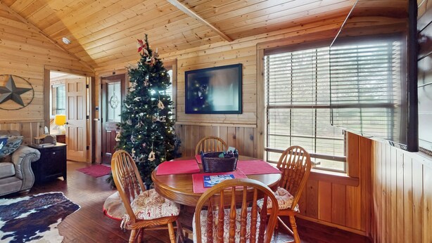 A cozy cabin interior with a wooden ceiling, a Christmas tree, a dining table with chairs, and a television on the wall. - Water-view Cabin w/ Front Porch, W & D, Streaming (Carmine)