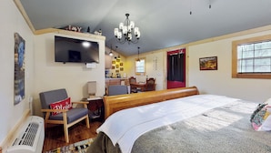 Ein Schlafzimmer mit Bett, Sessel, Fernseher, einer Deckenleuchte und einem Fenster.