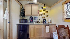 Eine kompakte Küche mit Holzausstattung, inklusive Kühlschrank, Mikrowelle, Kaffeemaschine und Spüle. An der Wand hängen Bilder in Rahmen und ein kleiner Weihnachtsbaum steht dort.