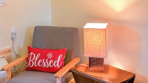Ein Stuhl mit einem roten Kissen mit der Aufschrift "Blessed" und ein Tisch mit einer strukturierten Lampe.