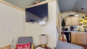 Ein gemütliches Wohnzimmer mit einem grauen Sofa, einem Holztisch und einem an der Wand befestigten Fernseher.