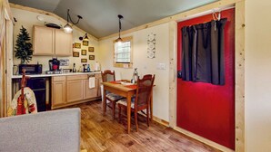 Una cucina compatta con mobili in legno, un tavolo da pranzo con sedie, un forno a microonde e una porta rossa.