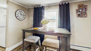 A small kitchen with a wooden table, two stools, a clock, and a window with curtains. - 12 Mi to Lake George! Quiet Adirondack Escape (Fort Ann)
