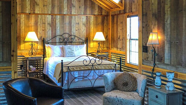 Une chambre dans une cabane en bois, avec un lit, deux lampes de chevet, une chaise et une table de chevet.