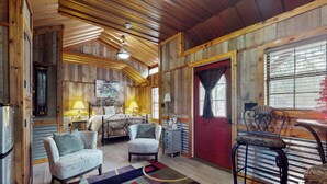 L’intérieur d’un chalet rustique, avec un plafond en bois, un lit doté d’une table de chevet, deux fauteuils, une table à manger et une porte rouge.